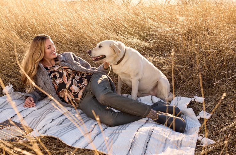 Fall Fashion 2023 woman laying in field on blanket with her dog